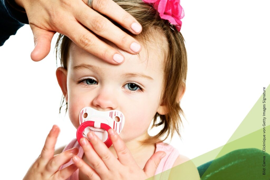 Bei einem krank aussehenden Kleinkind wird mit der Hand an der Stirn die Temperatur geprüft zum Thema Grippaler Infekt bei Kleinkindern: Homöopathie in der Erkältungszeit